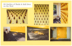 A large display window featuring 99 bottles of Rock & Roll Beer glued to the yellow wall about 10 inches apart. One of them has fallen onto the floor and has shattered.