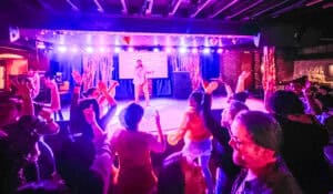 A crowd of people at karaoke with their hands up and someone singing on stage