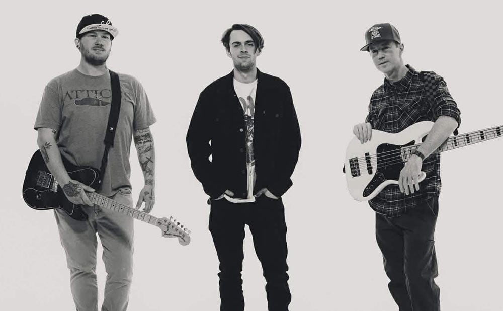 Three men stand against a plain background; the man on the left holds an electric guitar, the center man stands with hands in pockets, and the right holds a bass. This black-and-white image captures The Last Stanza at Blueberry Hill Duck Room on May 29th.